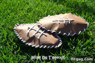 Finished brown paper footballs with white yarn laces, scattered on a vibrant green grass field, symbolizing victory and playtime