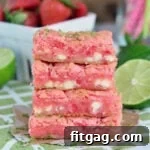 stacked strawberry gooey bars four high on green and white napkin with cut limes and fresh strawberries in background.