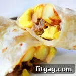 A breakfast burrito cut in half on a white plate, revealing the flavorful filling.