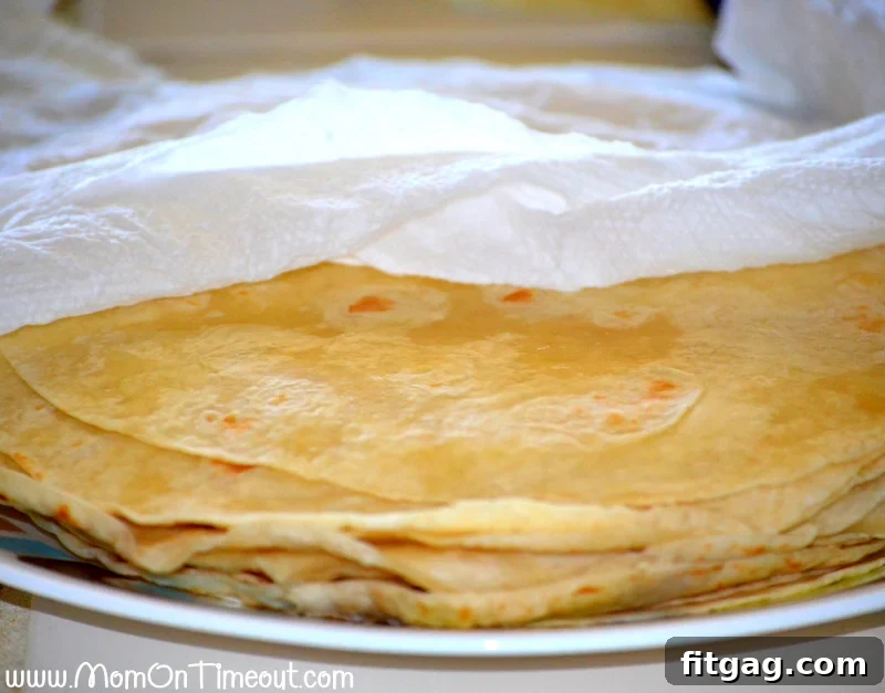 Stack of warmed flour tortillas wrapped in damp paper towels on a plate.