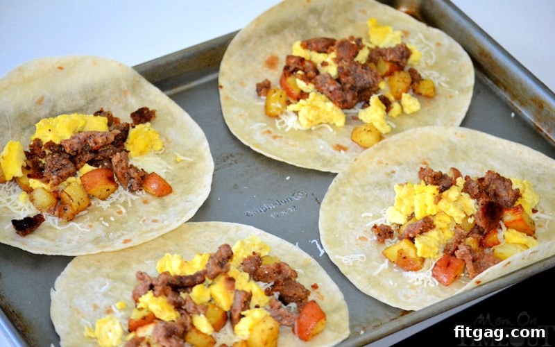 Four breakfast burritos being assembled with cheese, eggs, potatoes, and meat on tortillas.