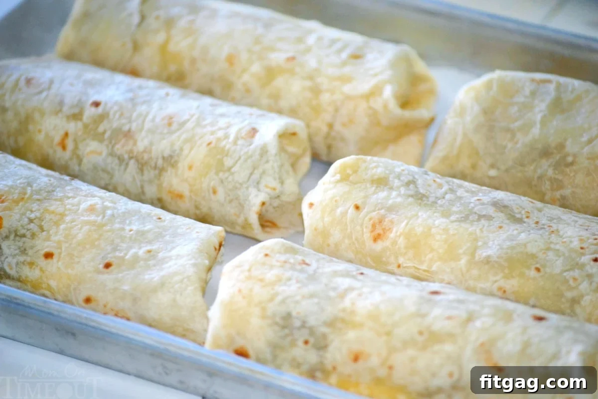 Six freshly assembled breakfast burritos laid out on a baking sheet for freezing.