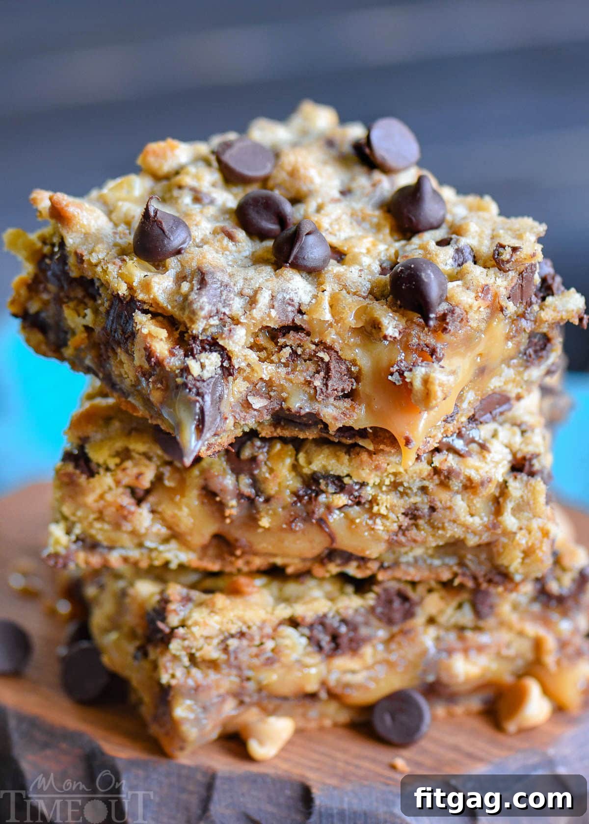 Three decadent peanut butter caramel toffee chocolate chip cookie bars stacked on a rustic wood board, showcasing their rich layers.