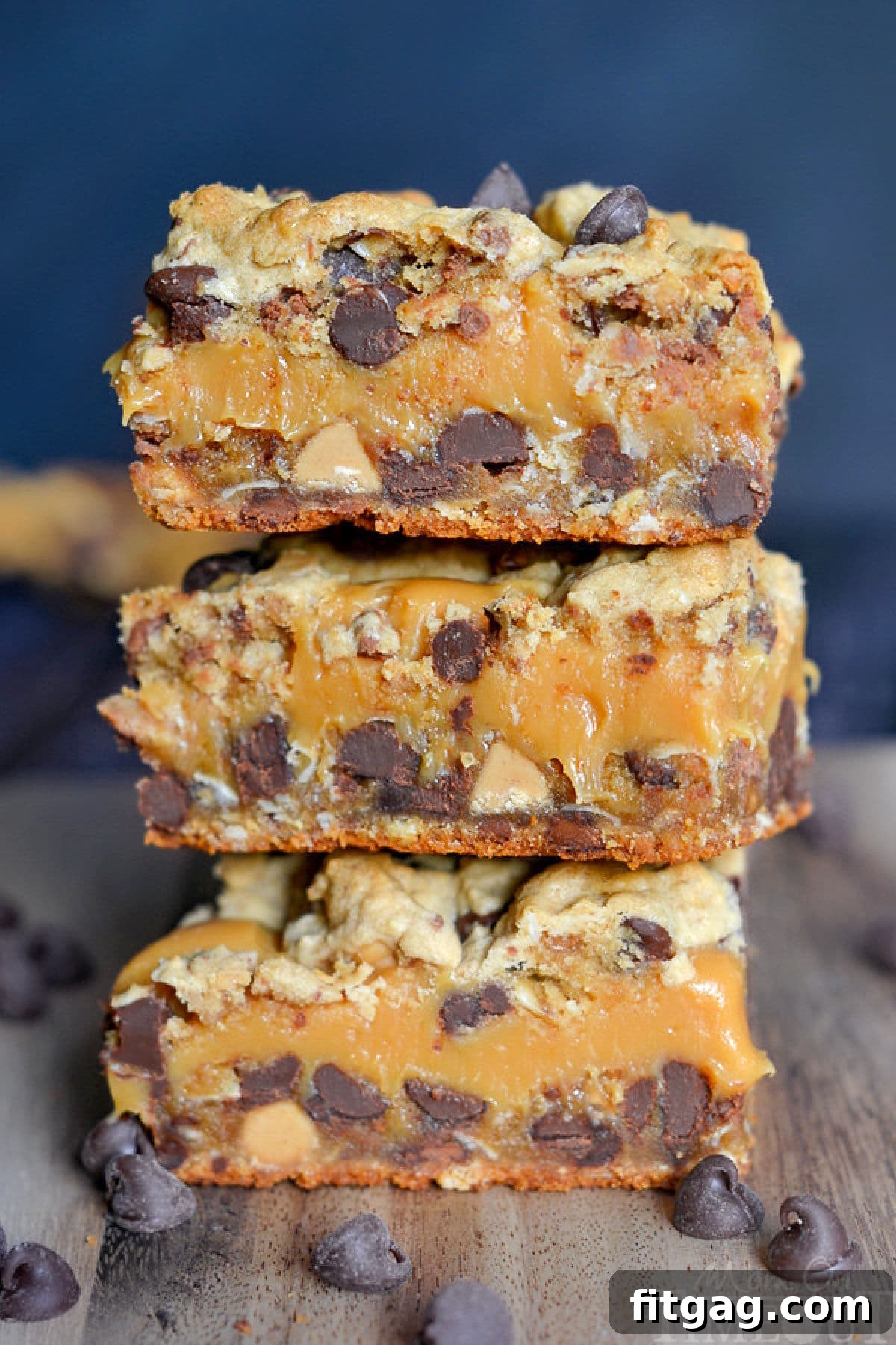 A close-up view of peanut butter caramel toffee chocolate chip cookie bars, freshly baked and stacked on a wood cutting board, highlighting the gooey caramel and crunchy toffee.