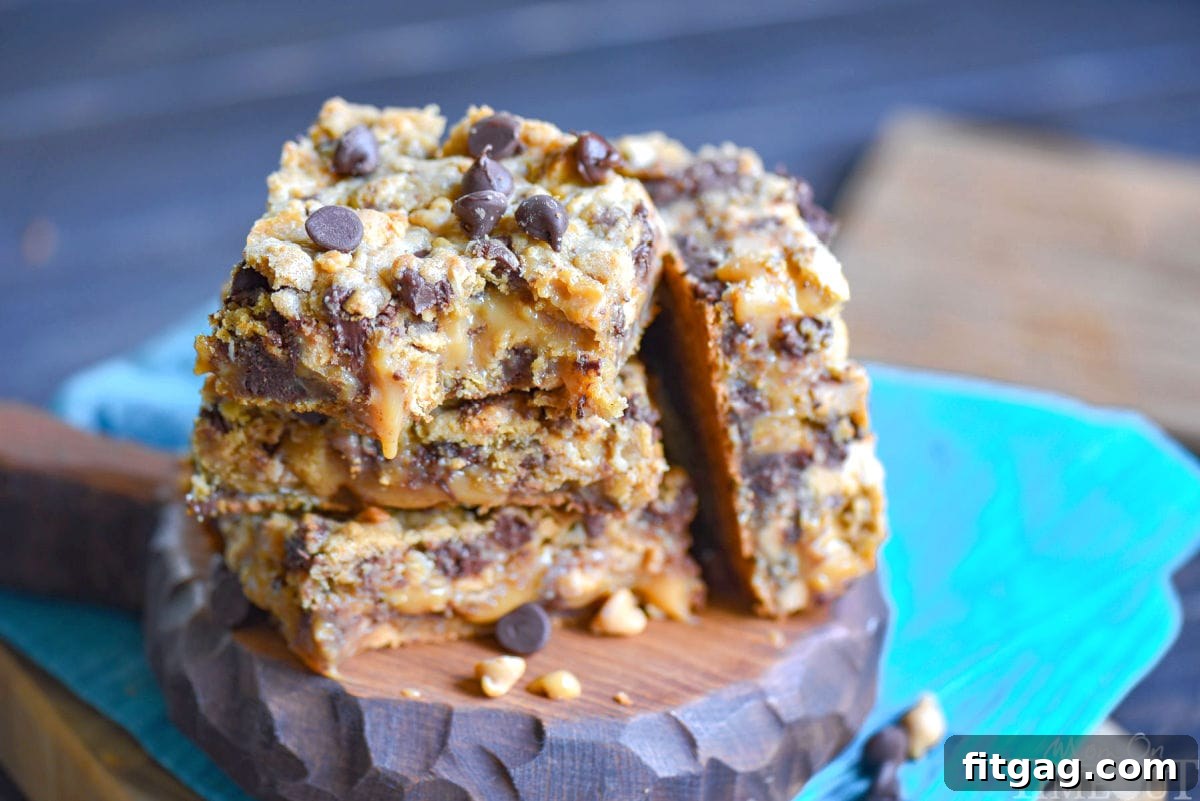Three perfectly cut Peanut Butter Caramel Toffee Chocolate Chip Oatmeal Cookie Bars stacked on a wooden board.