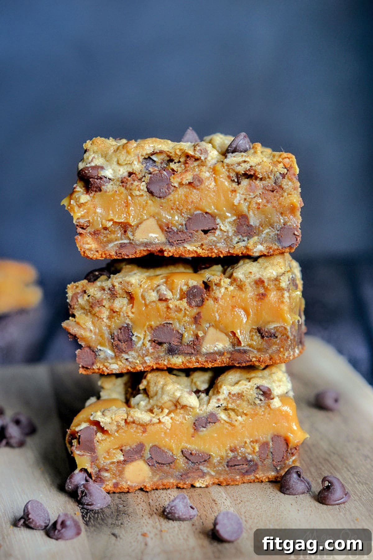 Peanut butter caramel toffee chocolate chip cookie bars neatly stacked on a wooden cutting board, ready to be enjoyed.