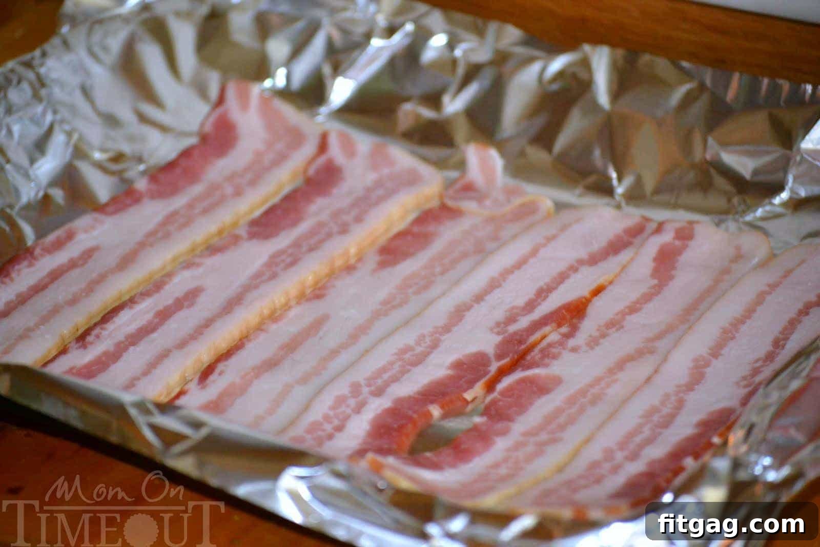 Bacon slices perfectly laid out in a single layer on a foil-lined baking sheet, ready for oven baking.
