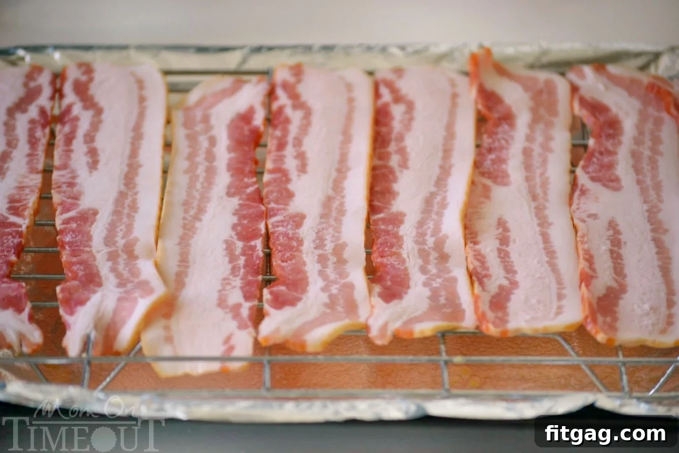 Raw bacon strips neatly arranged on an oven-safe cooling rack set within a baking sheet, preparing for perfect baking.
