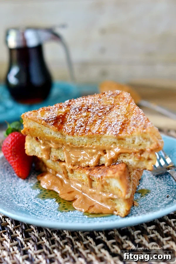 A stack of perfectly cooked Peanut Butter Stuffed French Toast, glistening with maple syrup and powdered sugar