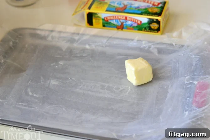 Preparing the base layer for S'mores Rice Krispies Treats Pinwheels: buttering waxed paper in a jelly roll pan before adding the cereal mixture.