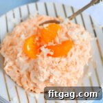 Refreshing orange jello salad topped with three mandarin orange slices, served on a gold striped plate.