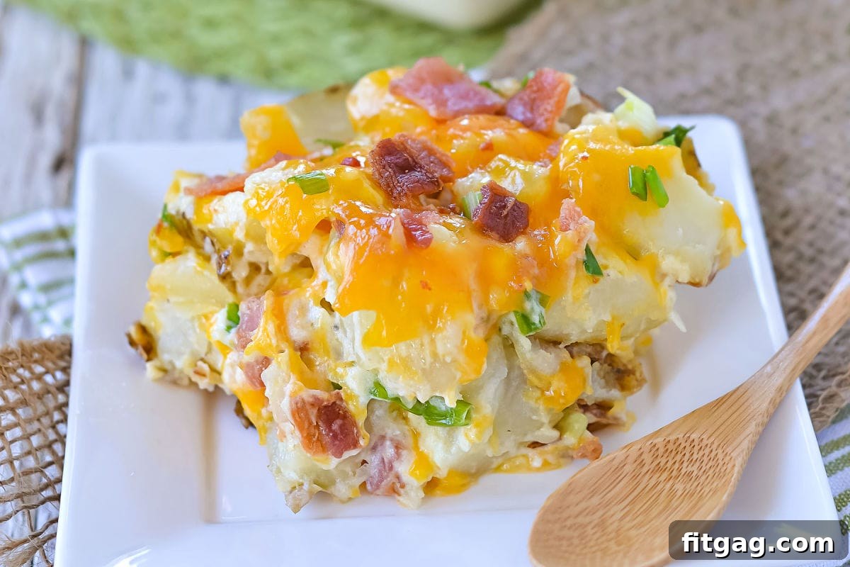 Close-up of potato casserole topped with shredded sharp cheddar cheese, crispy bacon, and fresh green onions, served on a small white square plate.