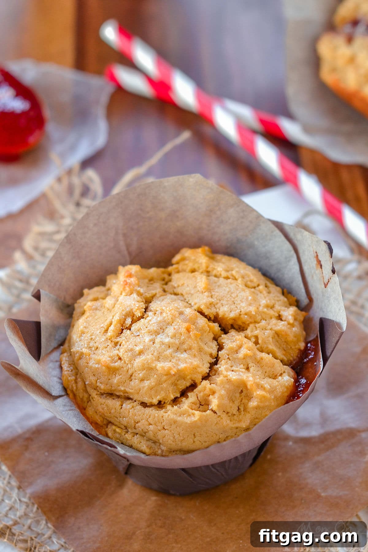 A single peanut butter muffin with a vibrant jelly center, resting in its parchment liner.