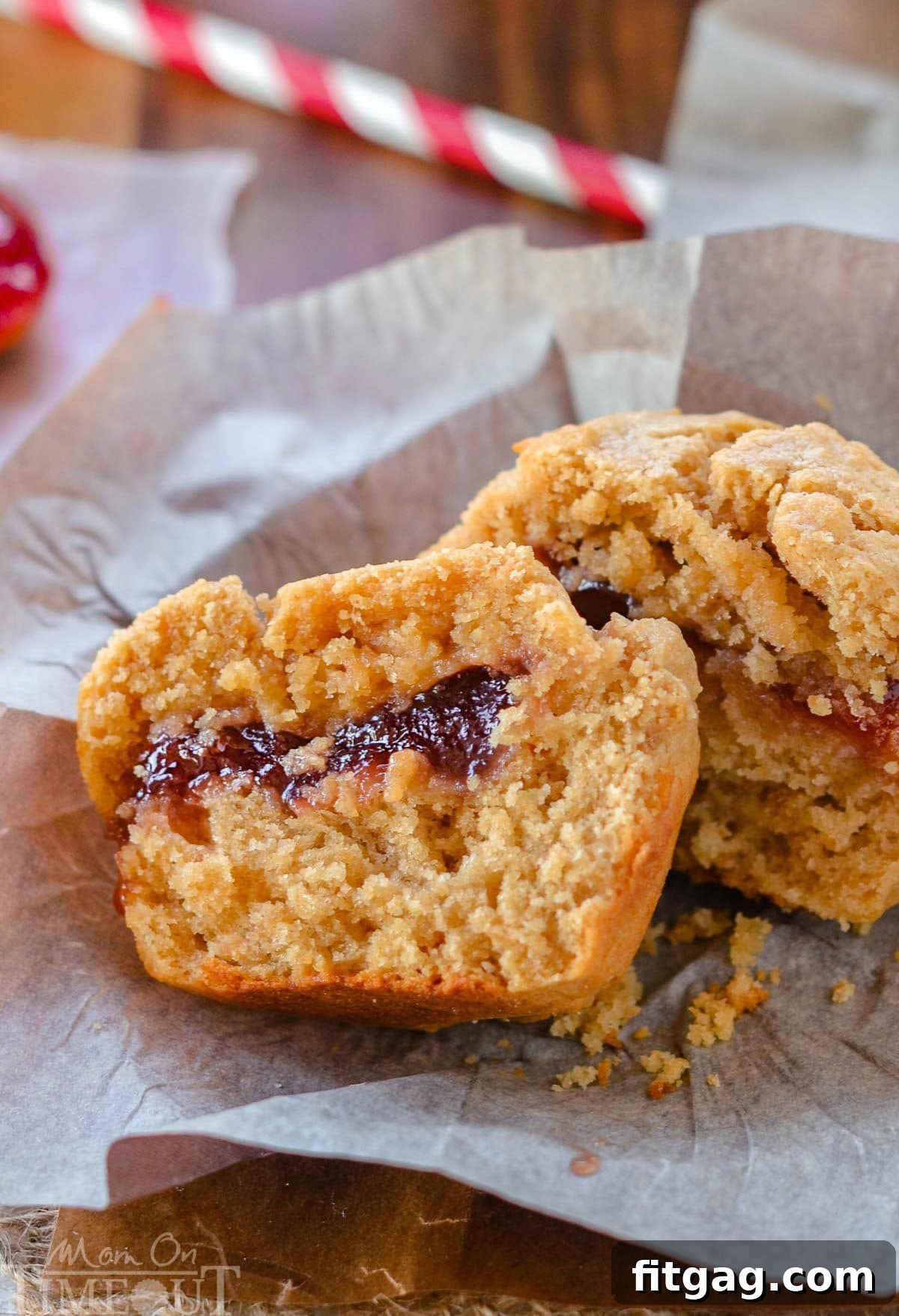 One peanut butter and jelly muffins on a piece of parchment. The muffin has been split in half to reveal the jelly center.