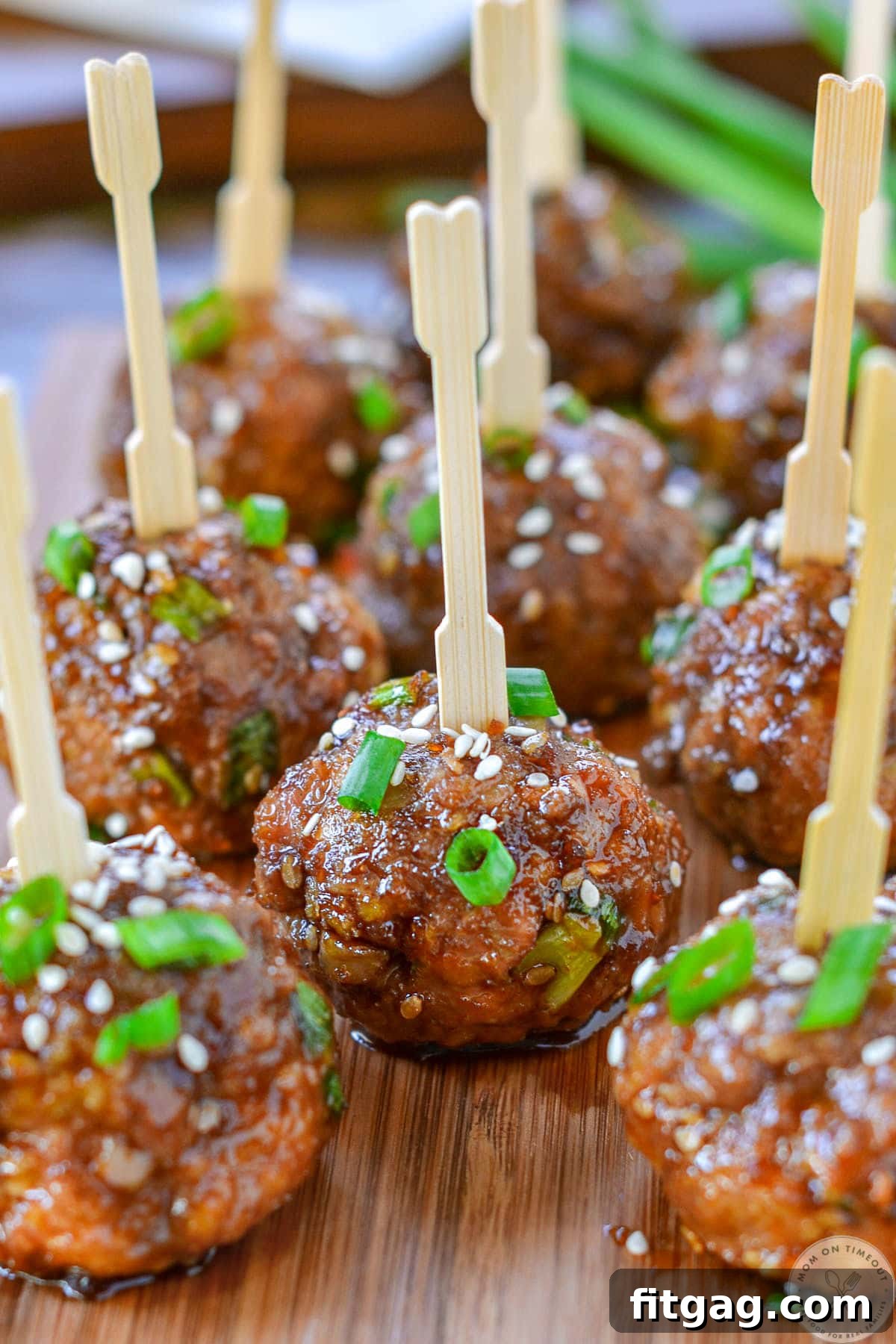 Glazed Teriyaki Meatballs 3 Close up of teriyaki meatballs on cutting board topped with white sesame seed and green onions.