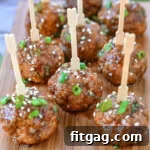 Nine teriyaki meatballs on wood cutting board topped with green onions and sesame seeds. Each meatball has a toothpick in it.