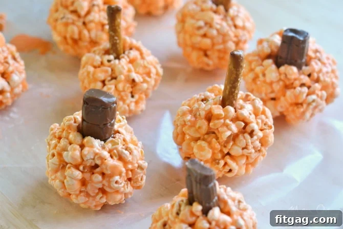 Autumn Pumpkin Popcorn Bites 4 Three perfectly formed Pumpkin Popcorn Balls adorned with candy leaves and pretzel stems, ready for holiday serving.
