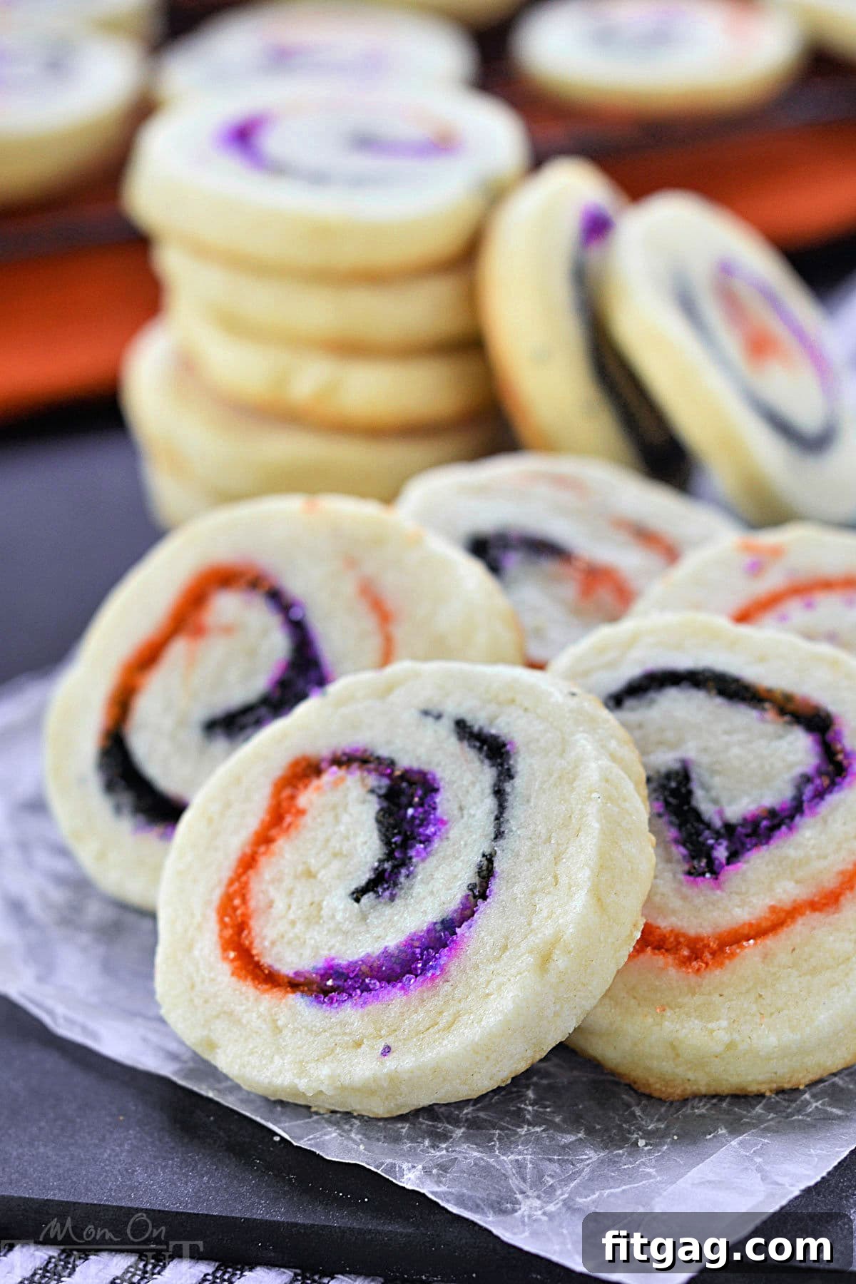 Halloween Sugar Cookies made with orange, black and purple sugar rolled into a spiral. A stack of cookies in the back and five cookies fanned out in the front to showcase the neat spiral design.