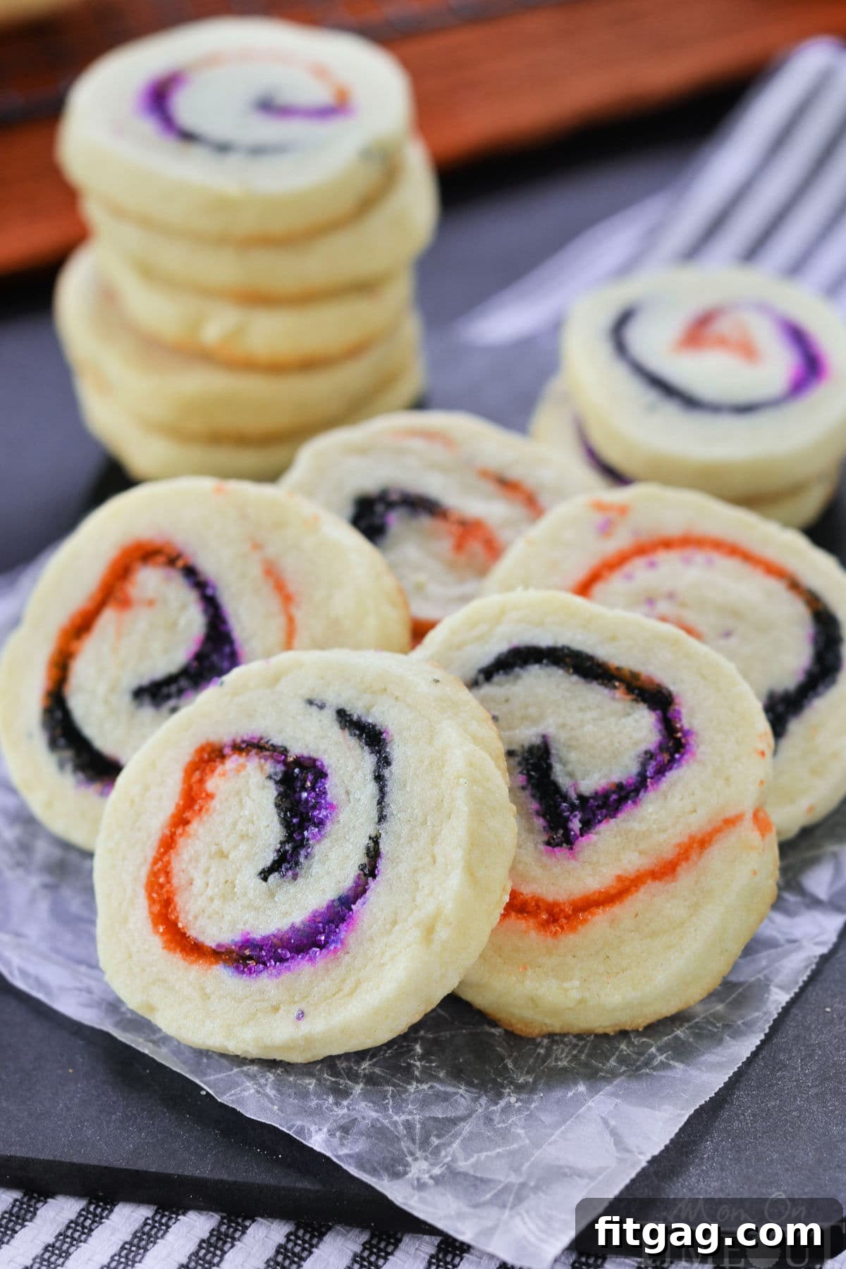 Halloween Sugar Cookies made with orange, black and purple sugar rolled into a spiral. A stack of cookies in the back and five cookies fanned out in the front to showcase the neat spiral design.