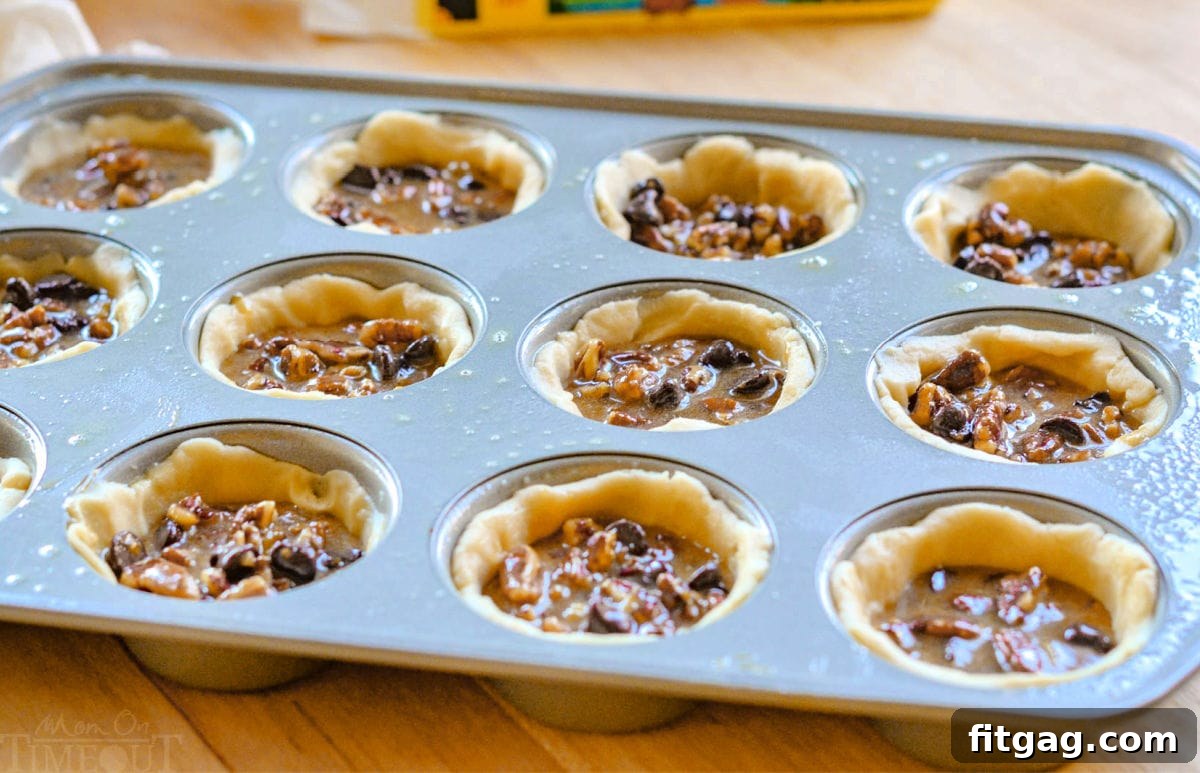 Pecan Pie Bites 4 A muffin tin filled with unbaked mini pecan pies, each featuring a golden crust and a rich, nutty filling topped with a pecan half, ready to be placed in the oven.