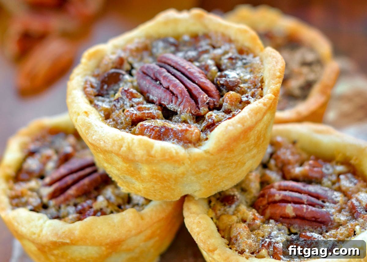 Pecan Pie Bites 6 A close-up shot of a single, perfectly baked mini pecan pie, showcasing its rich, glistening filling and a beautiful pecan half on top. The details of the flaky crust are visible.