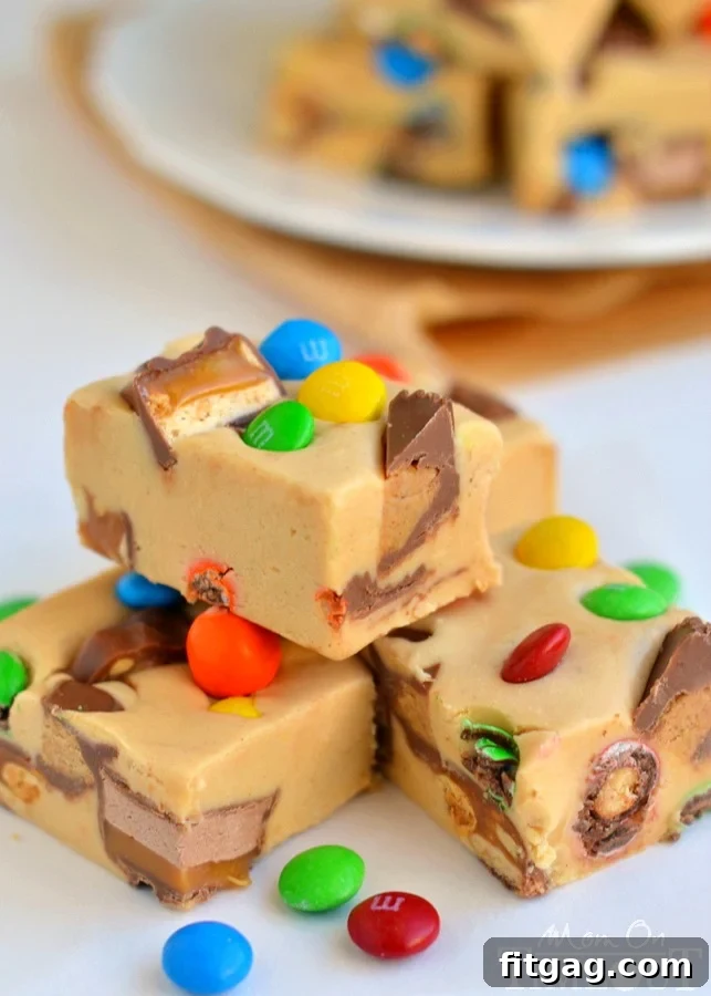 Three pieces of peanut butter candy bar fudge with a bite taken out of one, showcasing the mix of candies inside.
