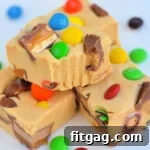 four pieces of peanut butter candy bar fudge stacked on white surface with bite taken out of top piece.