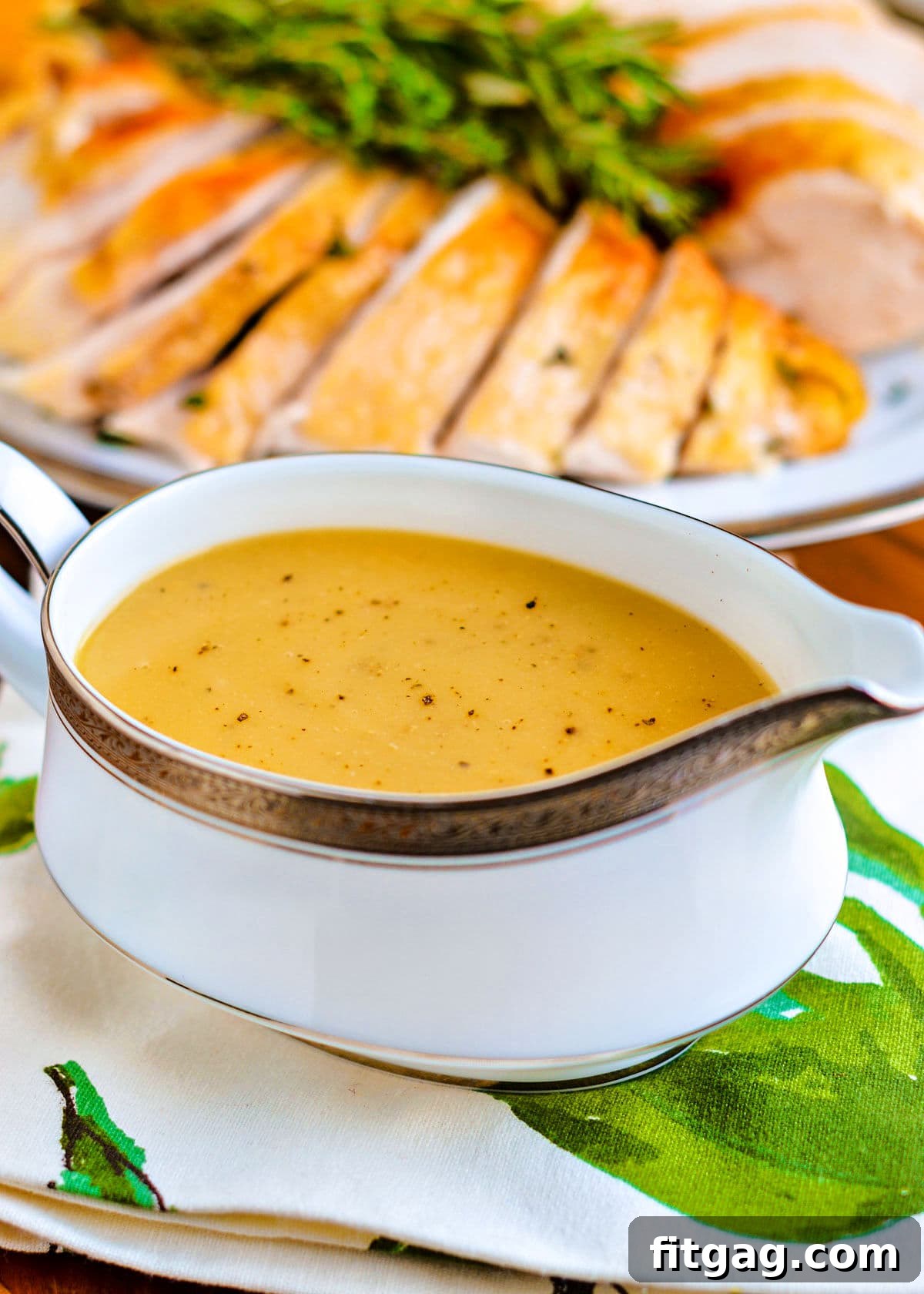 A beautiful gravy boat filled to the brim with rich, homemade turkey gravy, with a carved turkey subtly blurred in the background, ready for a festive meal.