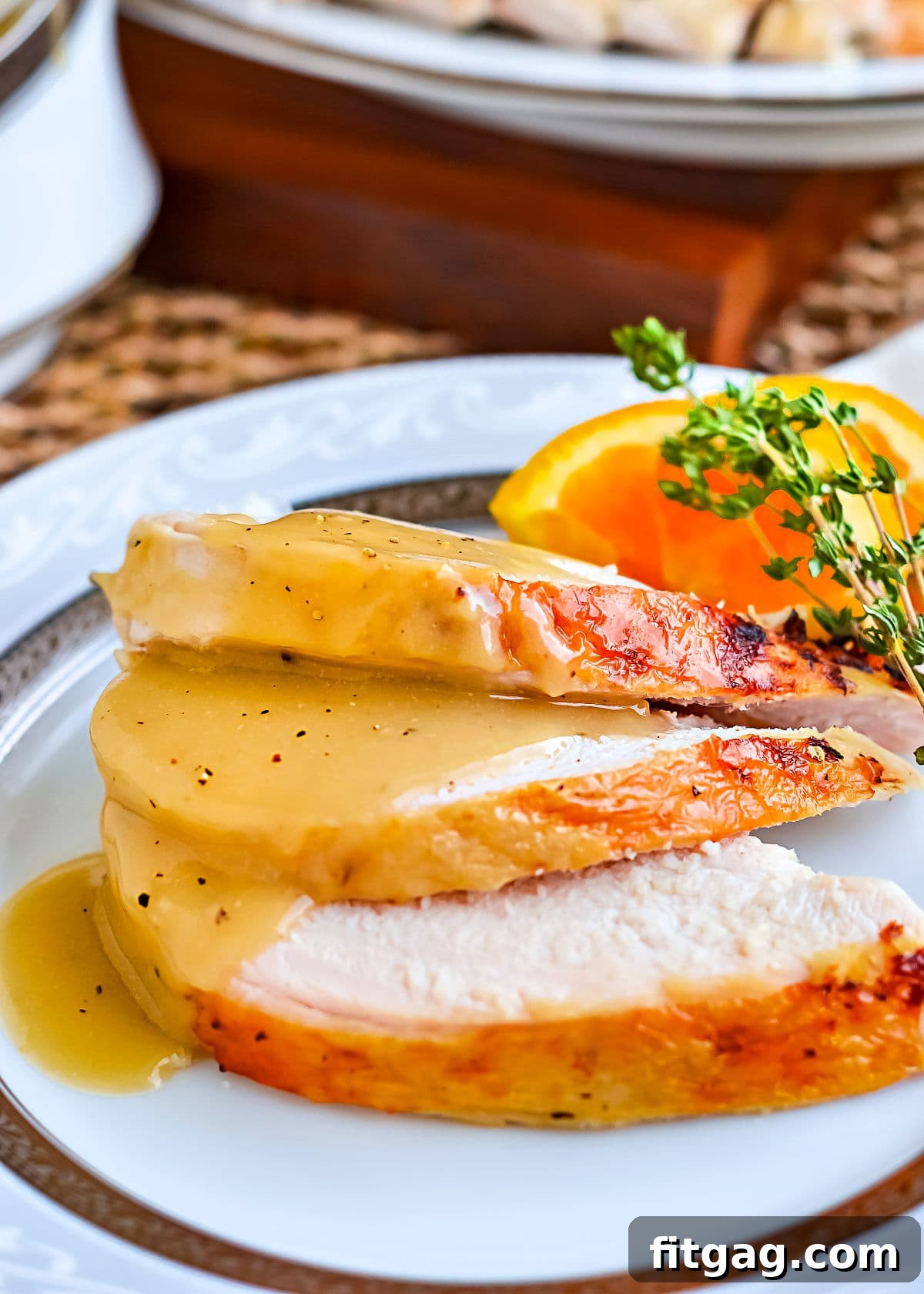 Three perfectly carved slices of juicy turkey breast, elegantly topped with a generous serving of silky smooth, rich brown turkey gravy, presented on a pristine white china plate with a delicate border.