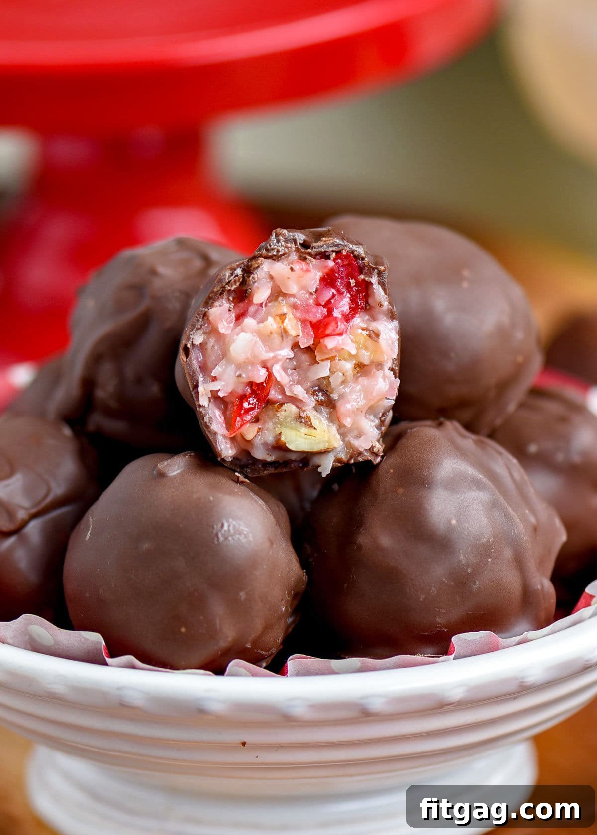 First Lady's Coconut Delights 5 A white bowl full of Martha Washington Candies, with one candy gently broken to showcase its rich, textured interior. A festive red stand is in the background.