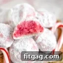 peppermint snowball cookie with bite taken sitting on top of a pile of more cookies with two candy canes on either siide