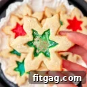 hand holding stained glass cookie over a plate of more cookies. centers are green and red.