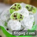 mint chocolate chip snowball cookies in a small green glass pedestal bowl lined with wax paper. A few cookies are broken in half to show the green interior and mini chocolate chips.