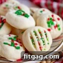 whipped shortbread cookies on a Christmas plate with red, green and white sprinkles. Plate is on cutting board sitting next to a Christmas towel.