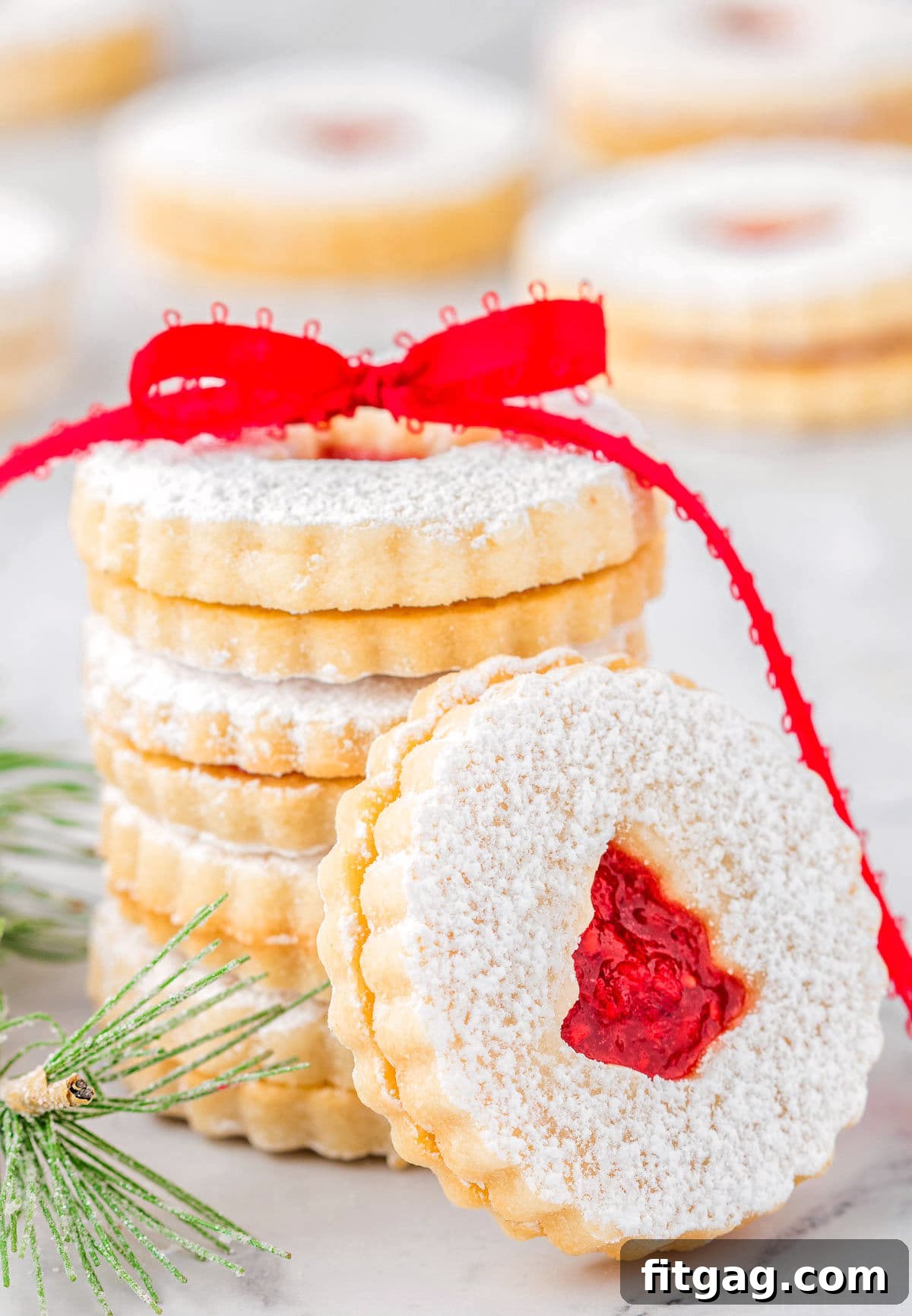 stack of linzer cookies with raspberry jam tied with red ribbon. one cookie is leaning up against the stack.