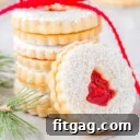 stack of linzer cookies with raspberry jam tied with red ribbon. one cookie is leaning up against the stack.