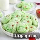 grinch cake mix cookies with red heart sprinkles sitting on white plate with milk jars in the background and Christmas ornaments scattered about.