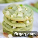 stack of four pistachio pudding cookies on white parchment studded with white chocolate chips and chopped pistachios.