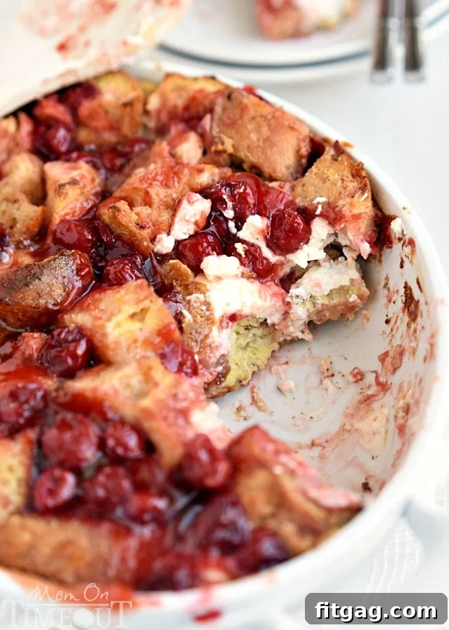 A close-up shot of the Baked Cherry Cheesecake French Toast Casserole, showcasing the gooey melted cream cheese and vibrant cherry filling peeking through the golden-brown bread cubes.
