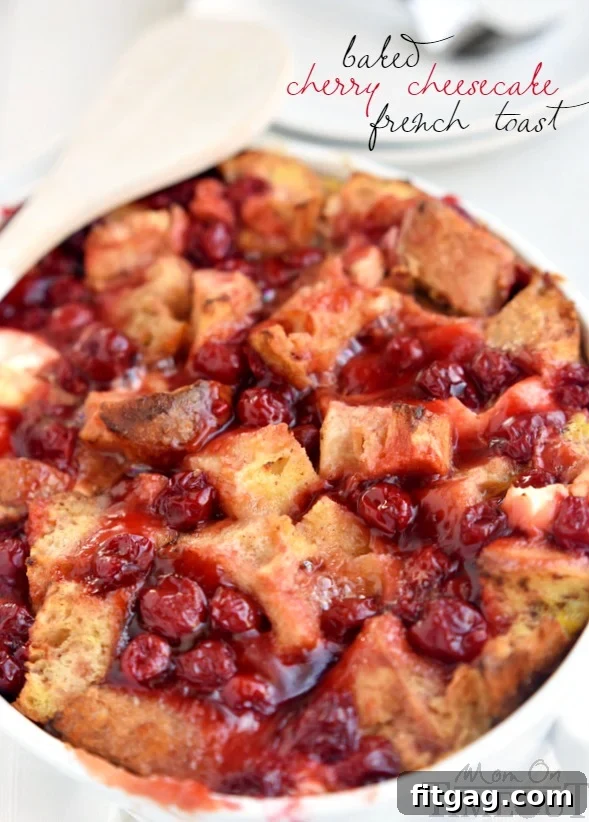 A single serving of Baked Cherry Cheesecake French Toast Casserole, perfectly portioned and ready to enjoy, dusted with powdered sugar and a side of fresh cherries.