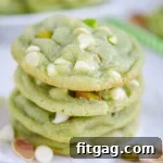 A stack of four soft pistachio pudding cookies on white parchment paper, featuring prominent white chocolate chips and chopped pistachios.