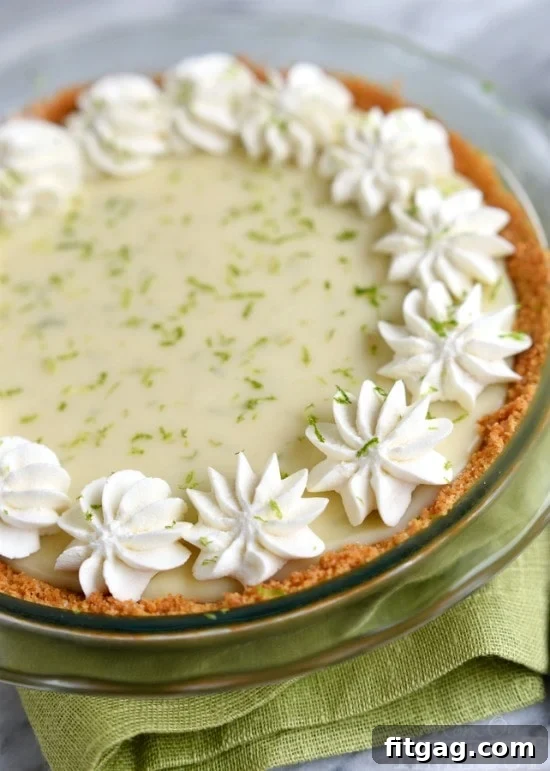 A slice of Key Lime Pie adorned with a generous swirl of homemade whipped cream and a sprinkle of fresh lime zest, ready to be enjoyed.