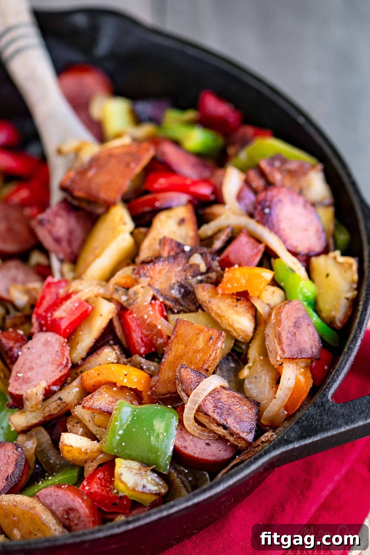 Kielbasa and potatoes in a cast iron skillet ready to be enjoyed. Skillet is resting on a red napkin. Peppers, onions, potatoes and kielbasa are all cut into bite sized pieces.