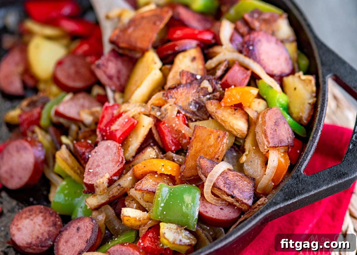 Kielbasa and potatoes in a cast iron skillet ready to be enjoyed. Skillet is resting on a red napkin. Peppers, onions, potatoes and kielbasa are all cut into bite sized pieces.
