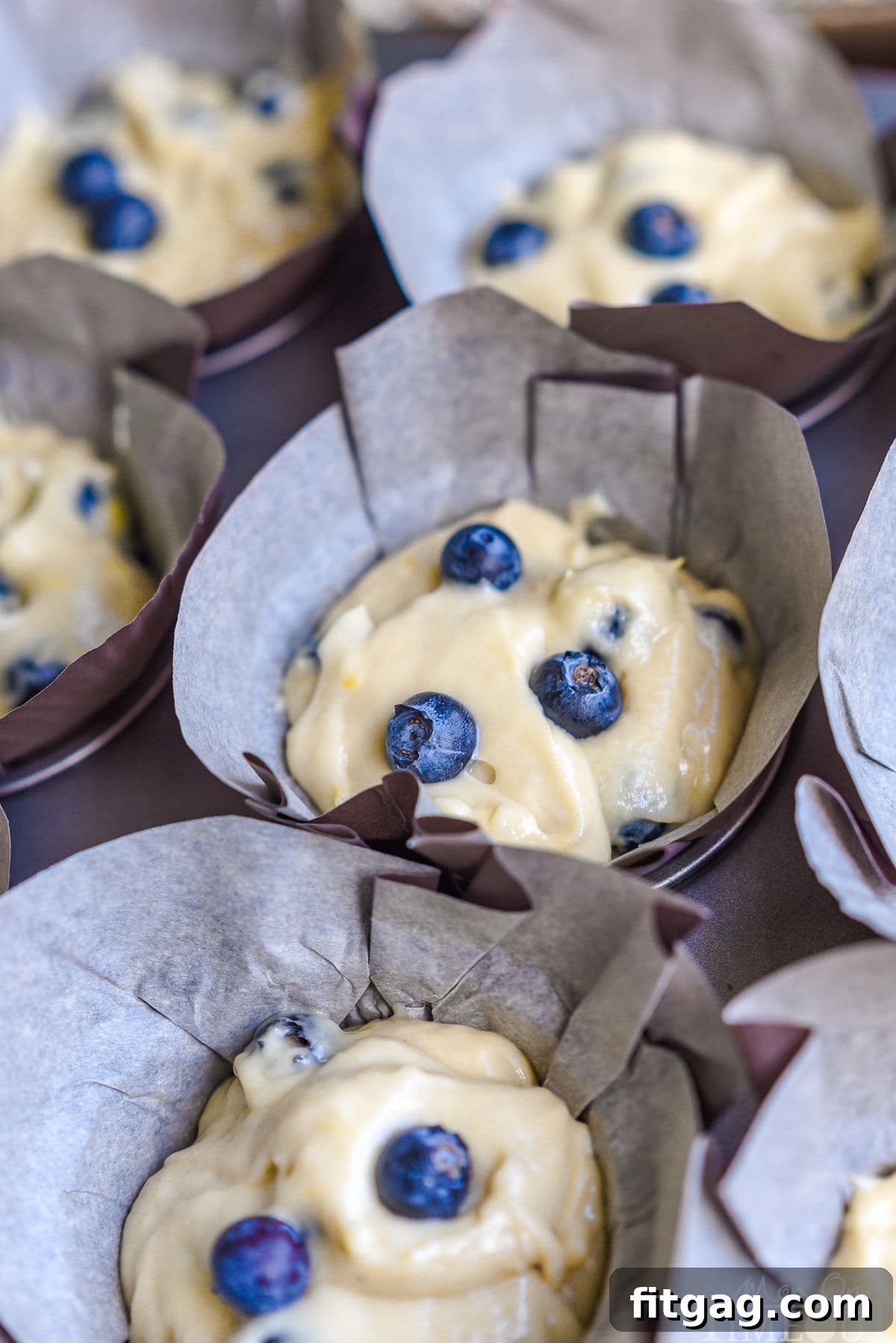 Muffin tin filled with Blueberry Lemon Cream Cheese Muffin batter in tulip parchment liners, ready to be baked to perfection.