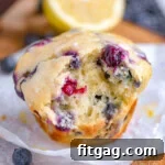 Blueberry muffin made with cream cheese and lemon sitting on white parchment with a bite taken out of the muffin. A lemon half can be seen in the background.