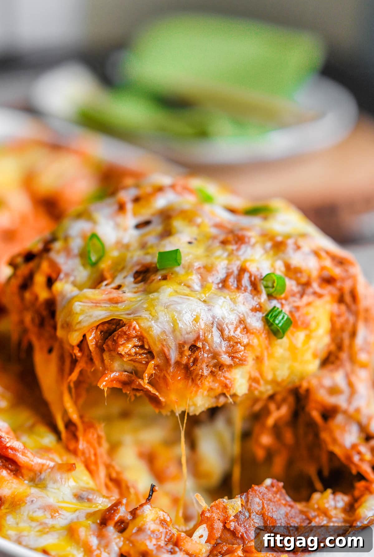 Loaded mashed potato casserole topped with pulled pork and melted cheese. A serving spoon has scooped a large portion from the baking dish, revealing the delicious layers.