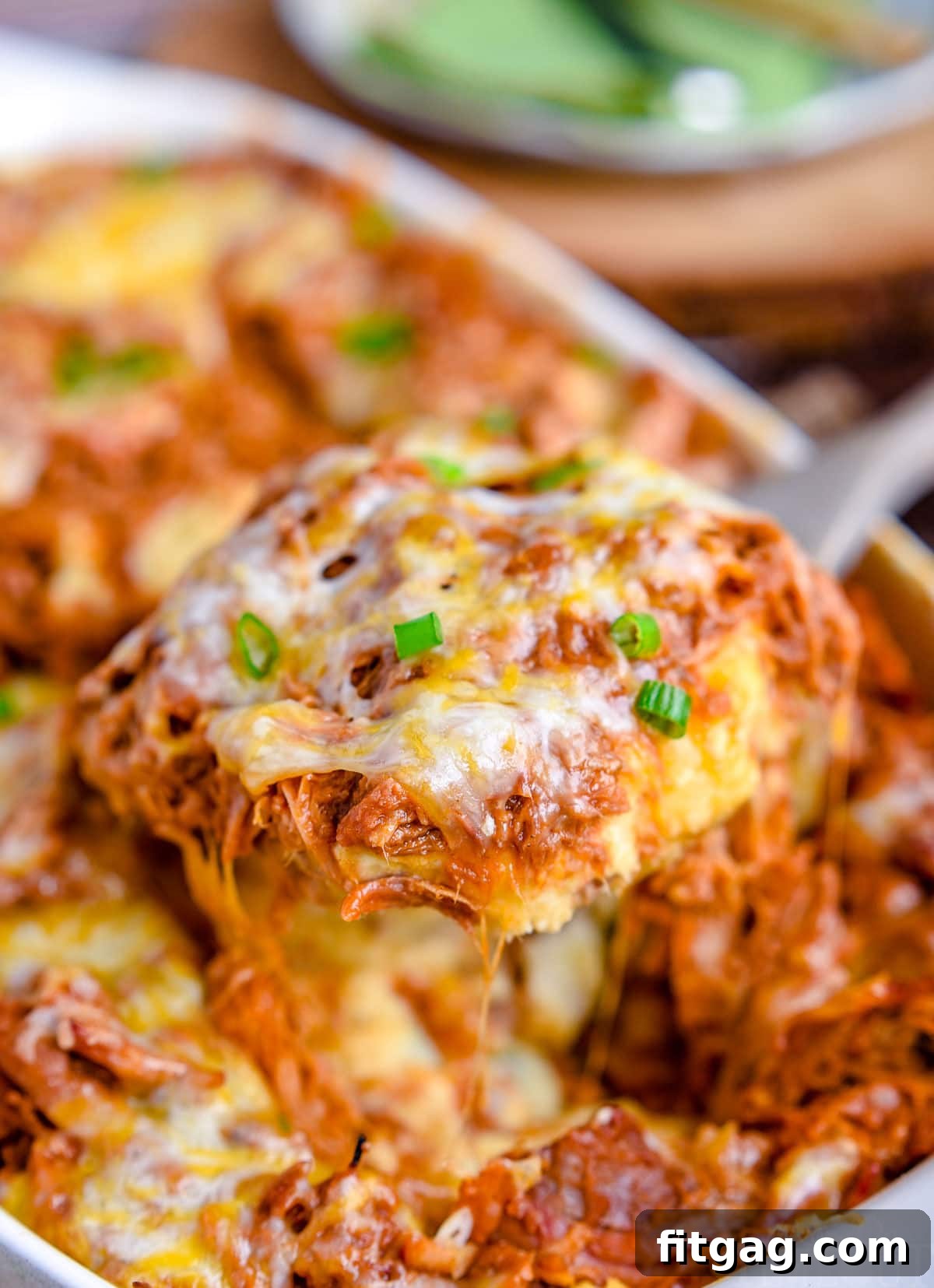 A large scoop of loaded mashed potato casserole with pulled pork and cheese being lifted from the baking dish, showcasing the layers.