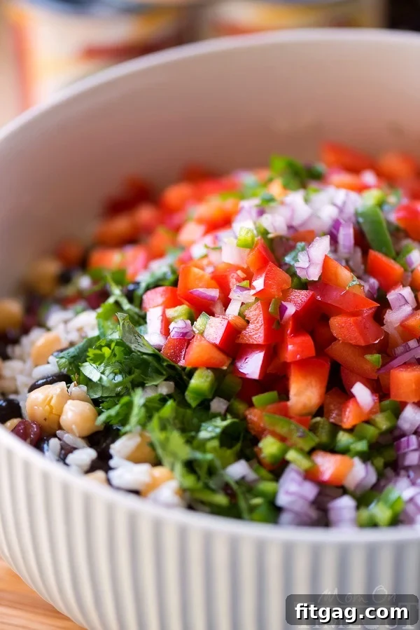 A large mixing bowl filled with vibrant vegetables and beans, including chopped bell pepper, red onion, cilantro, and jalapeño, ready to be combined for the salad