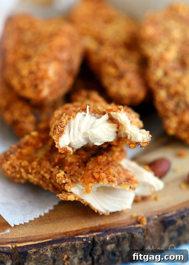 Spicy almond crusted chicken strips, one torn in half, showcasing the crispy crust and juicy interior on a wooden board.